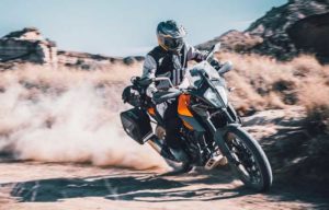 Ein Motorradfahrer fährt mit einem KTM-Motorrad über unbefestigten Gelände und wirbelt Staub auf.