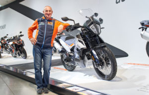 Ein Mitarbeiter von GST-Berlin GmbH steht lächelnd neben einem KTM-Motorrad in einem modernen Showroom.